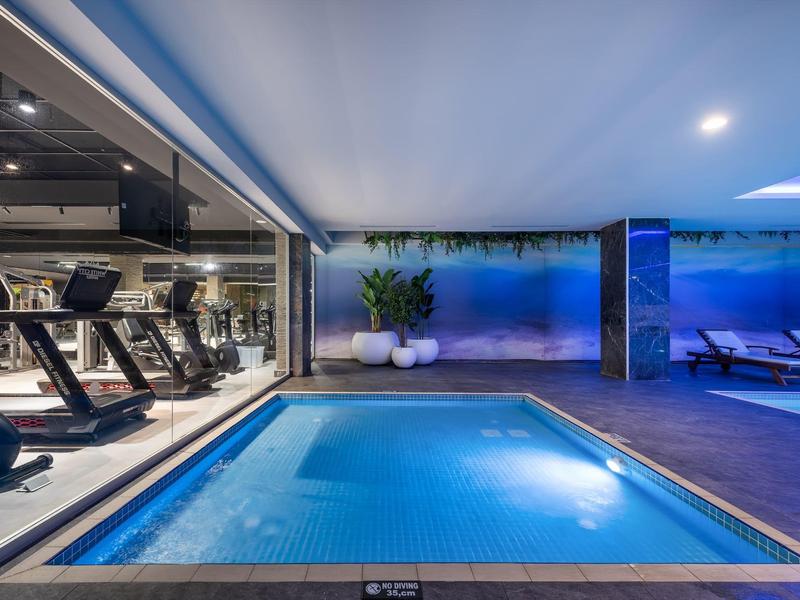 Modern overdekt zwembad met glazen ramen en fitnessruimte op de achtergrond.