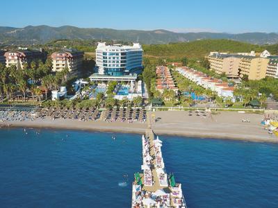 Pohled na pláž s dlouhým molem a několika hotelovými budovami v pozadí pod jasnou oblohou.