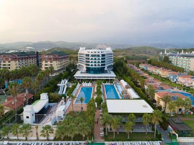 Velký hotelový resort s několika bazény, obklopený palmami a horami v pozadí.