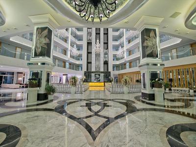 Velká hotelová lobby s mramorovou podlahou, centrálními výtahy a moderními posezeními.