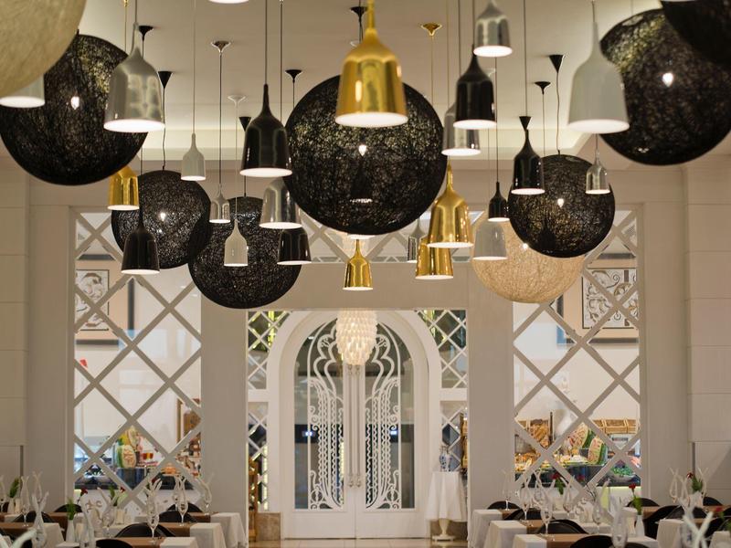 Elegantní hotelová jídelna s moderními černými a zlatými závěsnými lampami.
