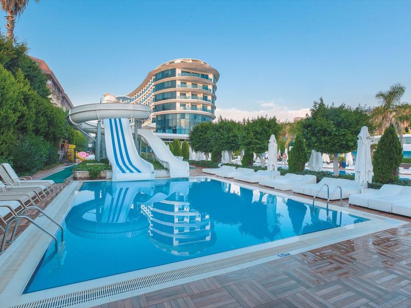 Hotelový bazén s tobogány a lehátky u moderního hotelu za slunečného dne.