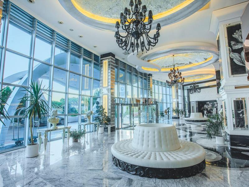 Světlá hotelová lobby s velkými okny, moderním sezením a lustry.