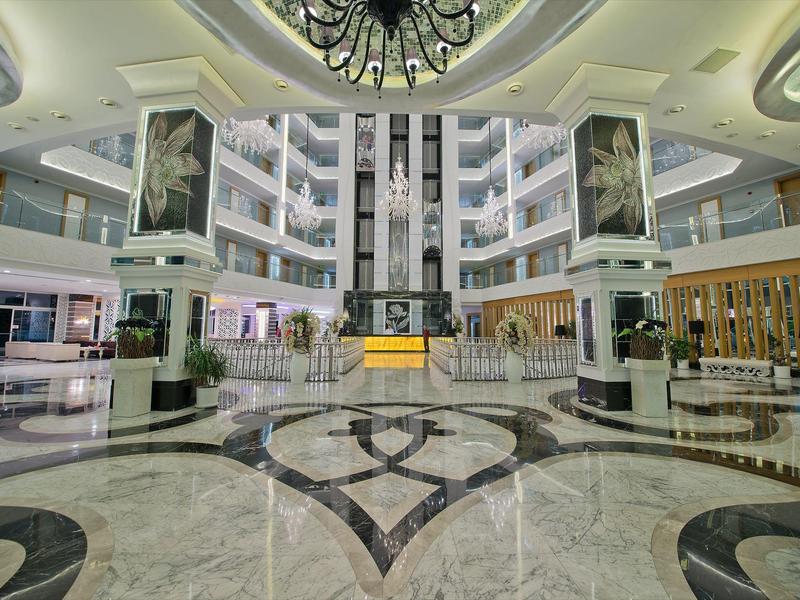 Velká hotelová lobby s mramorovou podlahou, centrálními výtahy a moderními posezeními.