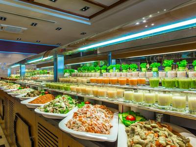 Buffet mit verschiedenem Gemüse, Salaten und Soßen in weißen Schalen und Gläsern auf langer Theke.