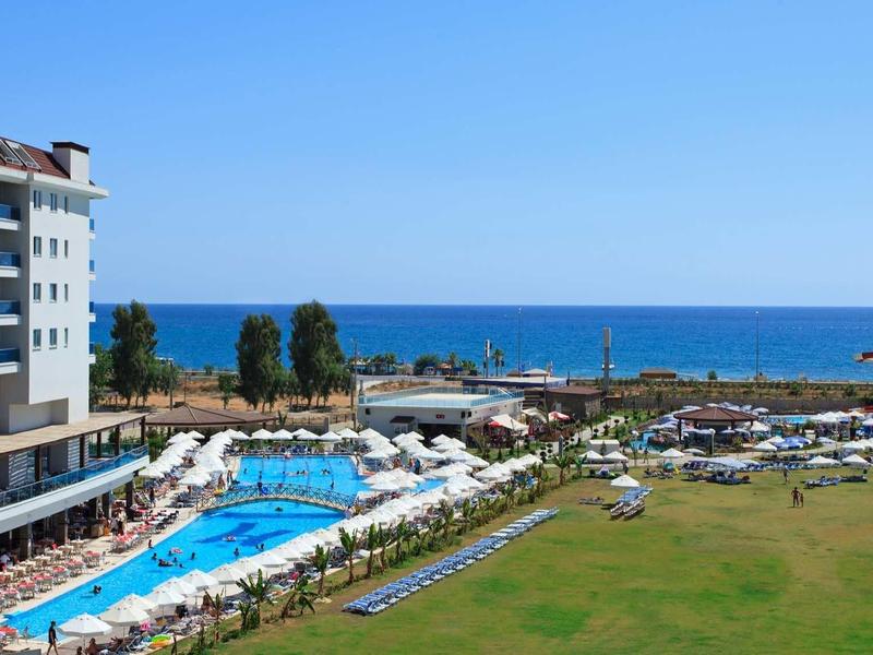 Hôtel en bord de mer avec piscine, pelouse verte et ciel bleu dégagé.