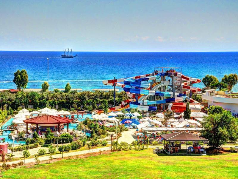 Vue d'un hôtel avec piscine et toboggans près de la mer, sous un ciel bleu clair.