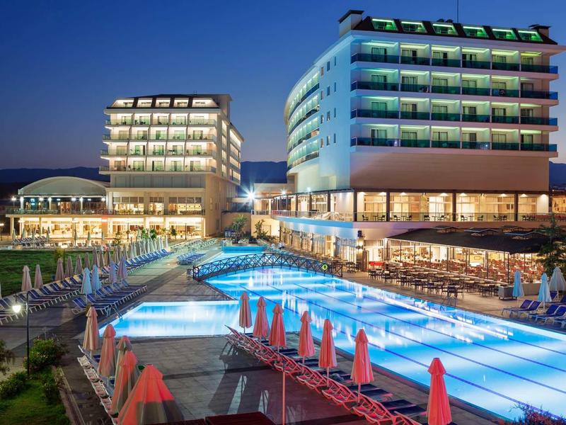 Complexe hôtelier moderne avec piscine extérieure éclairée et parasols rouges au crépuscule.