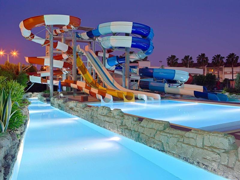 Parc aquatique avec toboggans colorés et piscine éclairée en soirée.