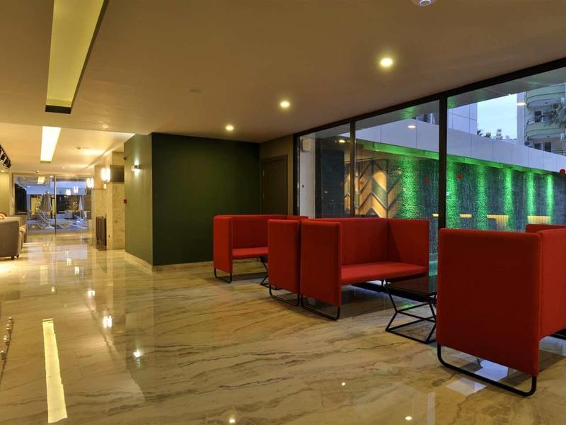 Modern hotel lobby with red armchairs, bar stools, and glass walls overlooking outside.