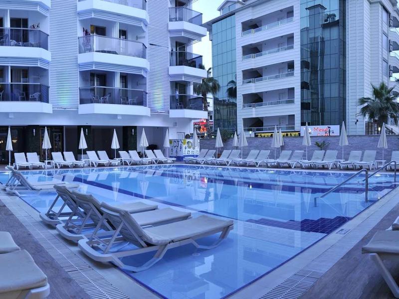 Modern outdoor pool with lounge chairs surrounded by multi-story hotel buildings at dusk