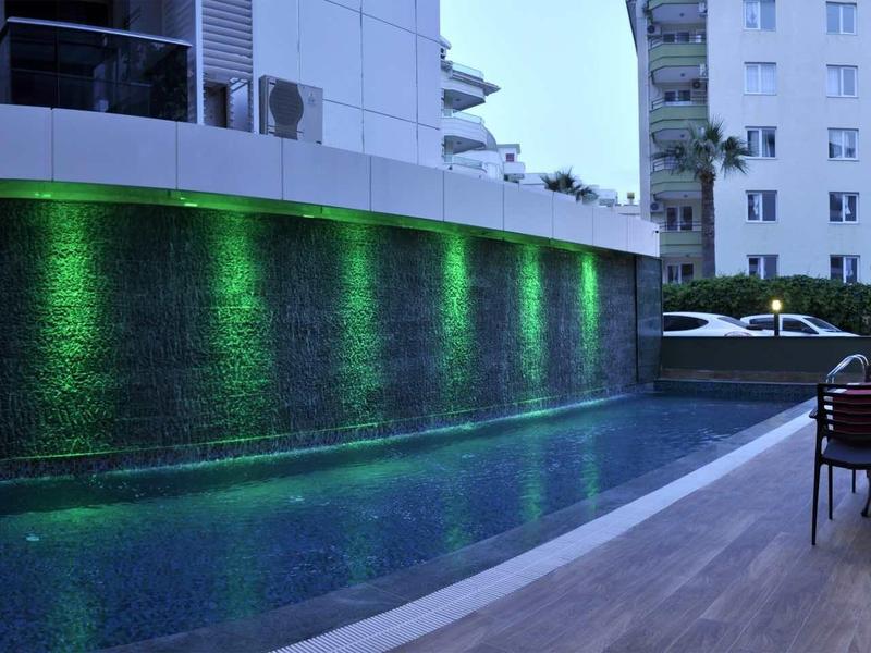 Modern outdoor pool with green lighting and seating area beside a hotel building.