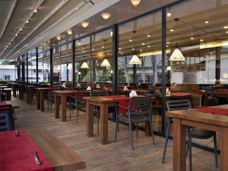 Modern hotel restaurant terrace with wooden tables and chairs under a covered area.