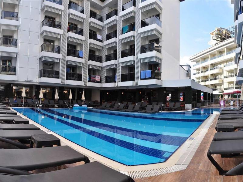 Modern hotel pool with lounge chairs and umbrellas outdoors under a blue sky.