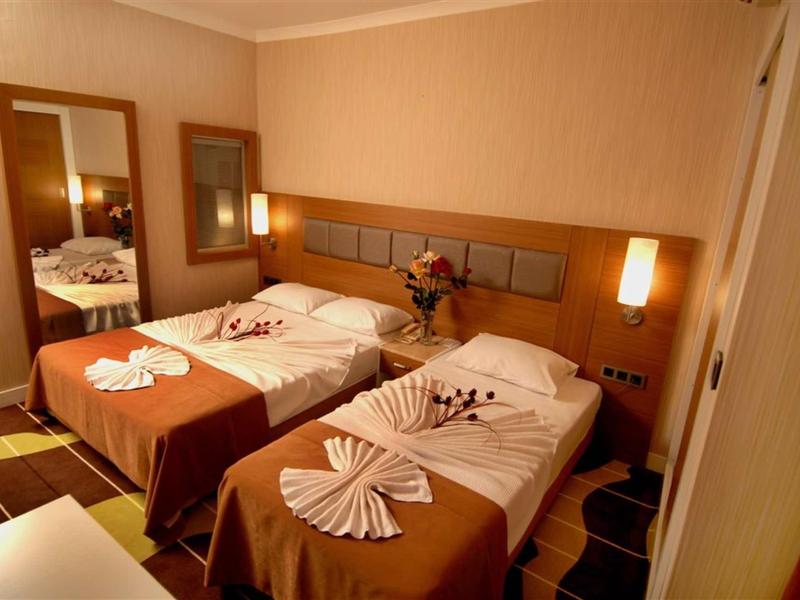 Hotel room with two beds, brown bedding, folded towels, and wall-mounted lamps.