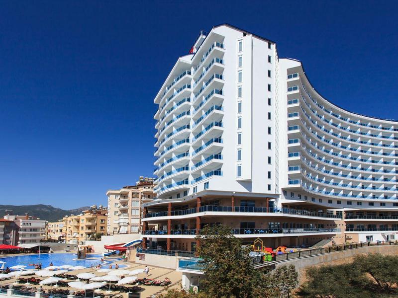 Edificio de hotel moderno con fachada curva bajo cielo azul claro y edificios cercanos.