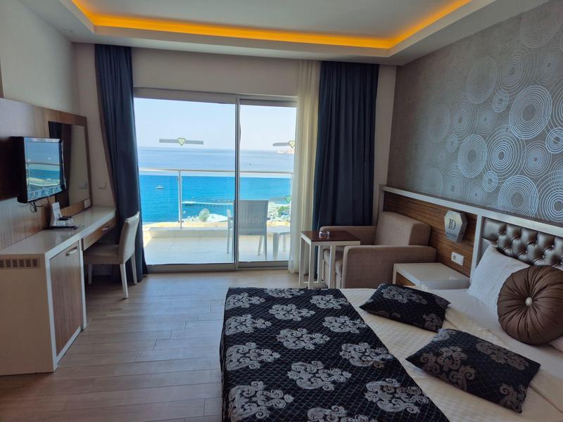 Habitación de hotel con cama doble, escritorio, silla y balcón con vista al mar a la luz del día.