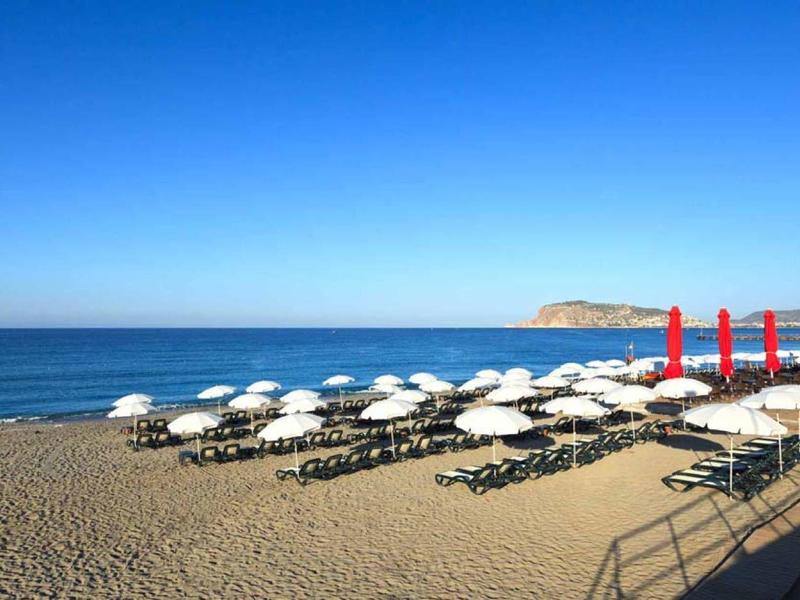 Playa con sombrillas y tumbonas junto a un mar tranquilo y cielo azul despejado.