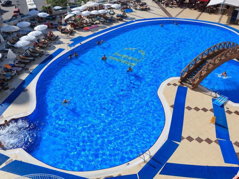 Gran piscina de hotel con agua azul clara, rodeada de tumbonas y sombrillas.