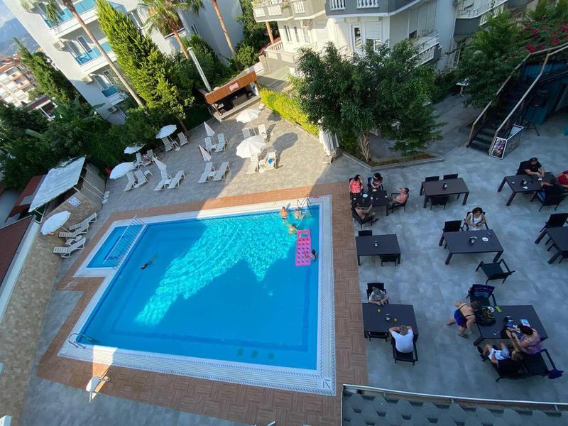 Busy outdoor pool area with guests at tables and loungers in a hotel complex.