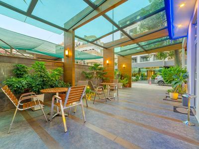 Venkovní hotelová terasa se sezením pod skleněnou střechou a rostlinami.