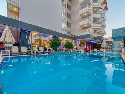 Moderní venkovní bazén s lehátky a slunečníky u hotelového komplexu.