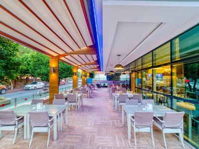 Moderní venkovní terasa hotelu s bílými židlemi a stoly pod markýzou.