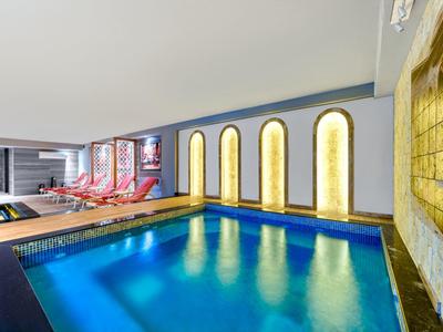 Vnitřní bazén s modrými dlaždicemi a lehátky vedle osvětlených stěnových nik.