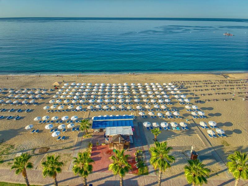 Pláž s řadami slunečníků a lehátek před klidným modrým mořem.