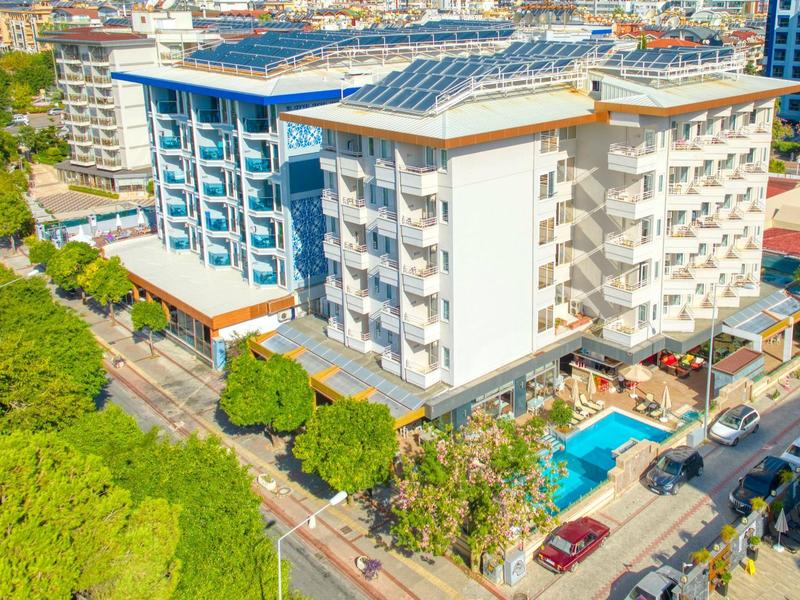 Moderní vícepodlažní hotel s balkónovými pokoji a venkovním bazénem v zeleném prostředí.