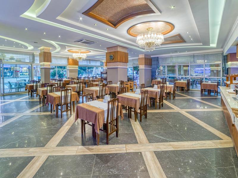 Prostorná světlá jídelna s kulatými a čtvercovými stoly a moderními lustry.