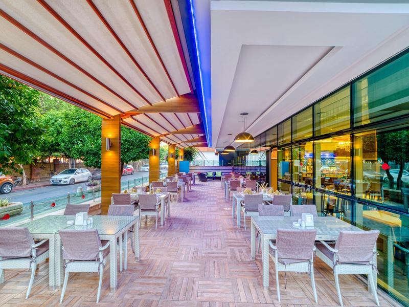 Moderní venkovní terasa hotelu s bílými židlemi a stoly pod markýzou.