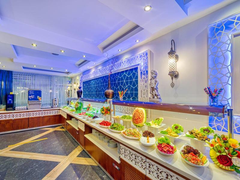 Bufet s různými čerstvými jídly a dekorativním modrým pozadím v hotelové restauraci.