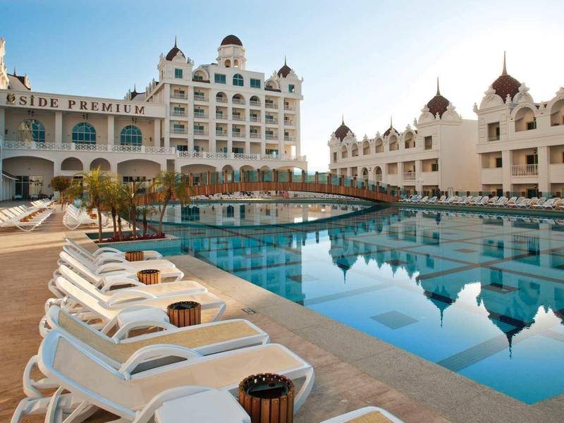 Large pool in front of a luxurious hotel with sun loungers and clear sky.