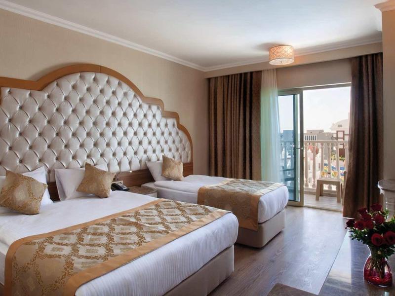 Elegant hotel room with two beds, tufted headboard, and balcony overlooking the sea.
