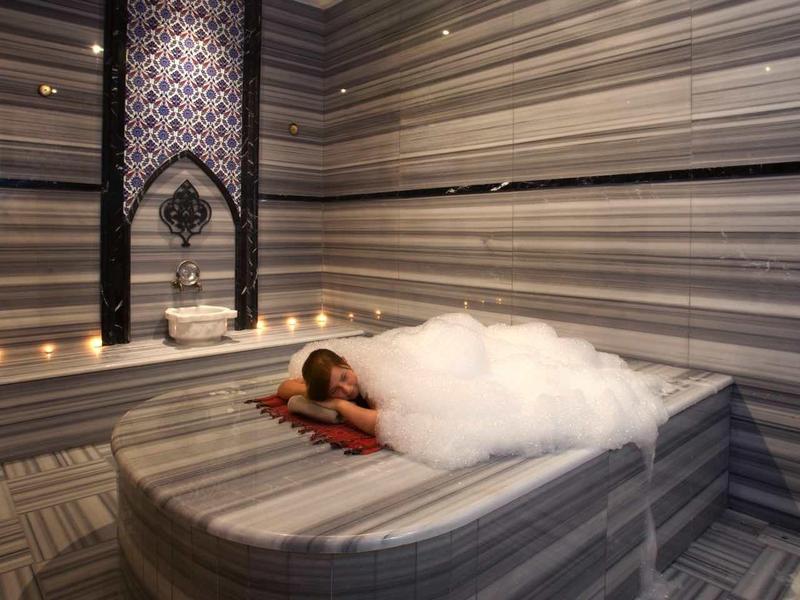 Person relaxing in a modern whirlpool in a striped wellness room.