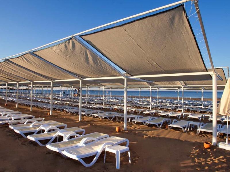 Beach with rows of white sun loungers under large sunshades by the sea.