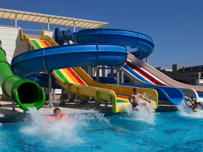 Several colorful water slides leading into a pool on a hotel rooftop.