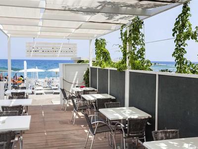Terrazza aperta con tavoli e sedie bianchi con vista sul mare e cielo blu.