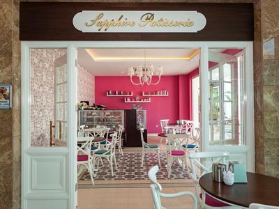 Inviting café with open entrance, white furniture, and pink wall in the hotel.