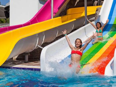 Two women laughing slide down a colorful water slide into the pool.