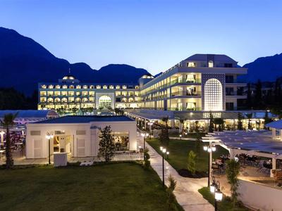Modern hotel with illuminated facades against mountain backdrop at dusk.