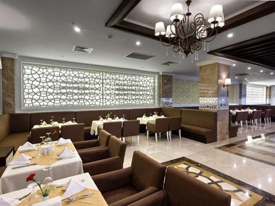 Modernes Restaurant mit braunen Sitzbänken, weißen Tischdecken und elegantem Kronleuchter.