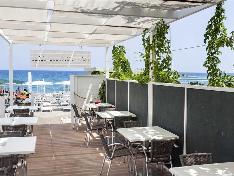 Cafe terrace with white tables and chairs, sea view.