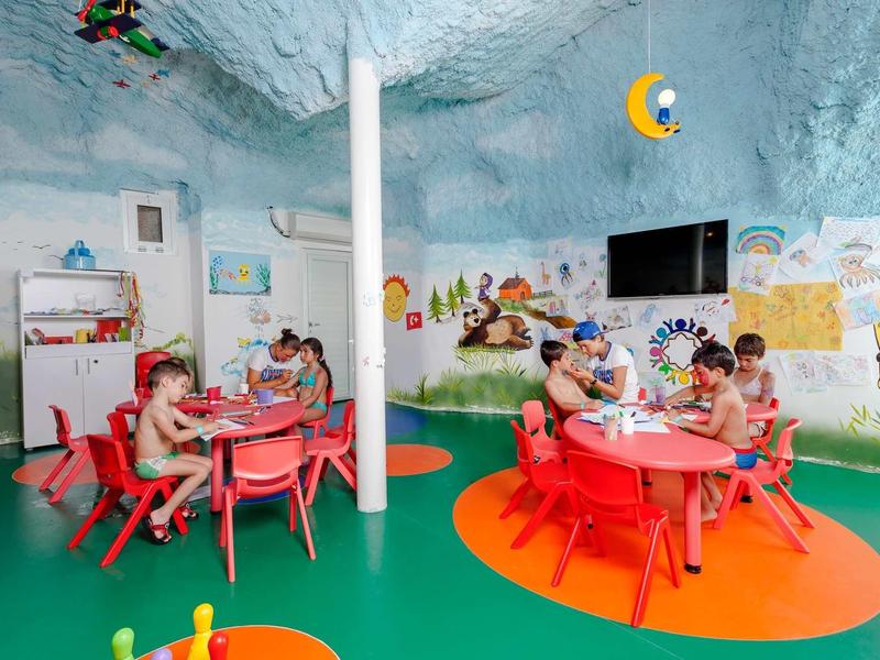 Children playing at small tables in a colorful, child-friendly room with wall murals.