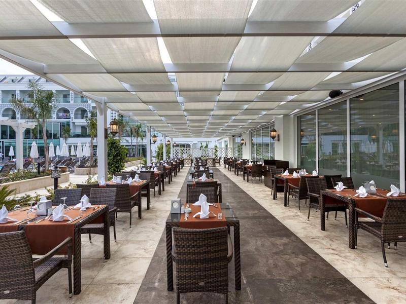 Covered outdoor terrace with set tables and brown chairs in hotel setting.