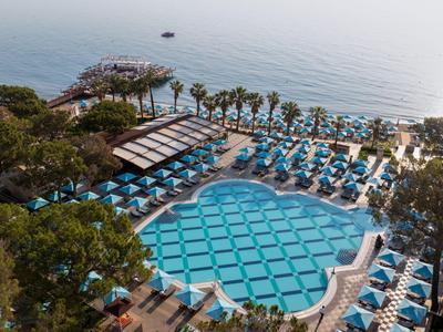 Großer blauer Hotelpool mit Liegen und Blick aufs Meer, umgeben von Palmen und Bäumen.