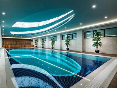 Innenpool mit blauer Wasserfläche, weißen Fließen und Pflanzen entlang der Wand.
