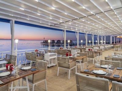Moderne Außenterrasse eines Hotels mit Tischen, Stühlen und Meerblick bei Sonnenuntergang.