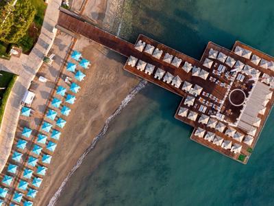Überblick über einen Strand mit Sonnenschirmen und einem Pier mit Liegen im Meer.